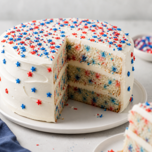This 4th of July cake recipe is festive, fun & totally ah-mazing! Red & blue velvet layers, cream cheese frosting & a candy surprise inside! 🎆